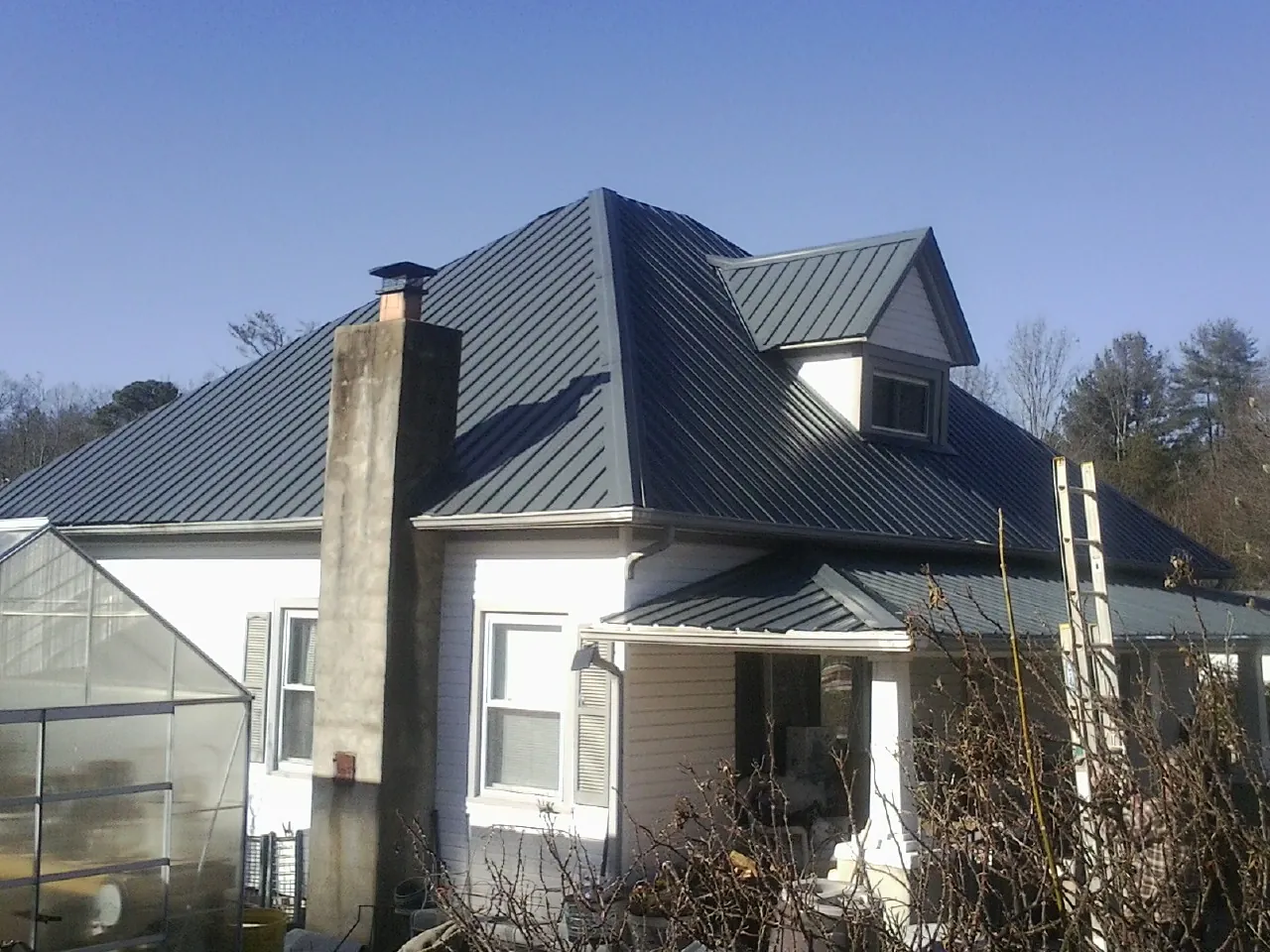 Dark blue standing seam metal roof on a white farmhouse with dormer — Slate & Tile Roof Repair by Roofing Brothers in Athol