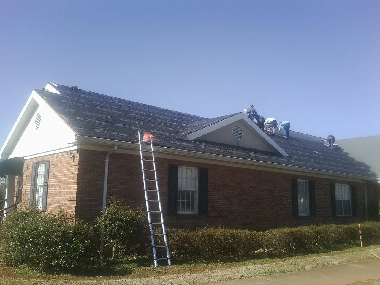 Crew tearing shingles off a brick ranch roof with a ladder set — Metal Roof Repair work by our crew in Athol