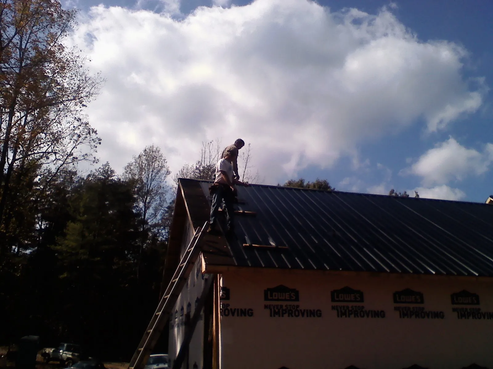 Roofer fastening dark metal panels high against a cloudy sky, from a Roof Inspection job in Athol